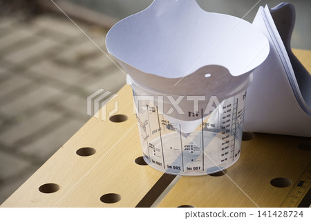 Clear Plastic Measuring Cup With Paper Funnel on Wooden Workbench for Paint Mixing and DIY Projects 141428724