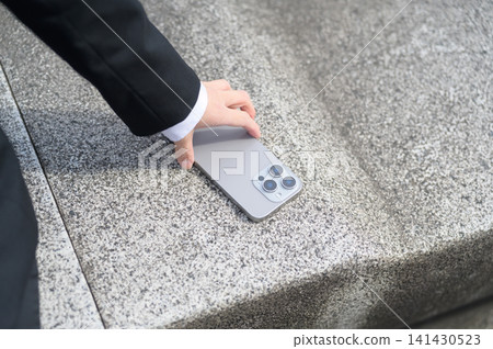 在商業場景中，有人從長椅上拿起自己的智慧型手機。 141430523