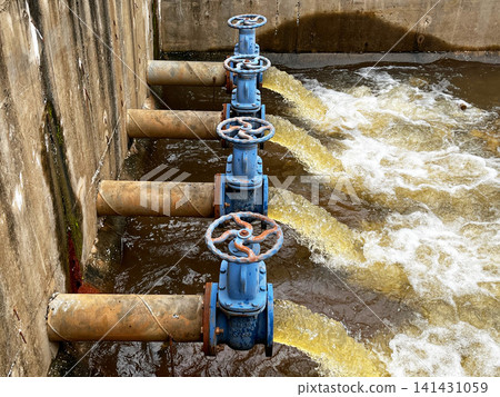 Industrial wastewater discharge facility close up, showcasing heavy duty blue control gate valves regulating brown effluent flow rate, hydraulic fluid pressure, and environmental drainage Industrial wastewater discharge facility close up, showcasing heavy duty blue control gate valves regulating brown effluent flow rate, hydraulic fluid pressure, and environmental drainage 141431059