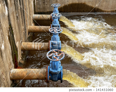 Industrial wastewater discharge facility close up, showcasing heavy duty blue control gate valves regulating brown effluent flow rate, hydraulic fluid pressure, and environmental drainage Industrial wastewater discharge facility close up, showcasing heavy duty blue control gate valves regulating brown effluent flow rate, hydraulic fluid pressure, and environmental drainage 141431060