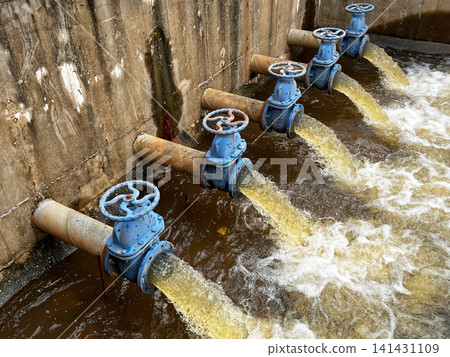 Hydraulic engineering system discharging liquid effluent, showcasing rusted blue gate valves controlling volumetric flow rate, hydrodynamic fluid pressure, and environmental drainage mechanism Hydraulic engineering system discharging liquid effluent, showcasing rusted blue gate valves controlling volumetric flow rate, hydrodynamic fluid pressure, and environmental drainage mechanism 141431109