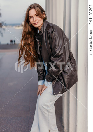 Woman leather jacket urban portrait of a stylish young female model posing against a white textured wall near the waterfront Woman leather jacket urban portrait of a stylish young female model posing against a white textured wall near the waterfront 141431262