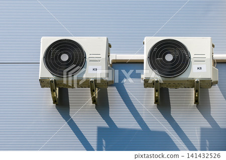 Twin outdoor HVAC air conditioning condenser units mounted on insulated industrial building facade wall Twin outdoor HVAC air conditioning condenser units mounted on insulated industrial building facade wall 141432526