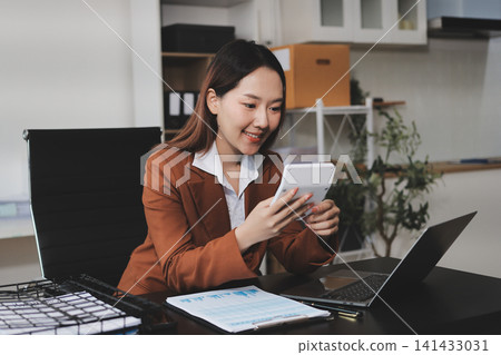 Asian businesswoman using calculator and working on laptop at modern office Asian businesswoman using calculator and working on laptop at modern office 141433031