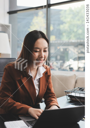 Asian businesswoman using calculator and working on laptop at modern office Asian businesswoman using calculator and working on laptop at modern office 141433036