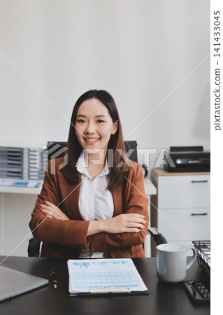Young Asian professional business woman calculating finances and analyzing data charts on computer, smiling while working on accounting project in a modern office, planning budget Young Asian professional business woman calculating finances and analyzing data charts on computer, smiling while working on accounting project in a modern office, planning budget 141433045