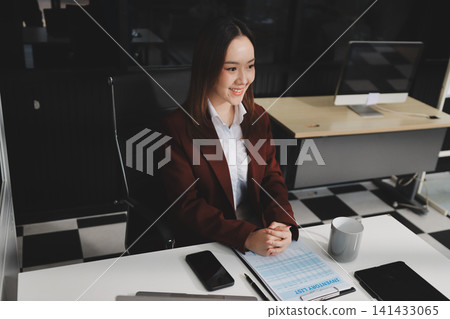 Smiling asian businesswoman talking on phone and using laptop while working at office desk Smiling asian businesswoman talking on phone and using laptop while working at office desk 141433065