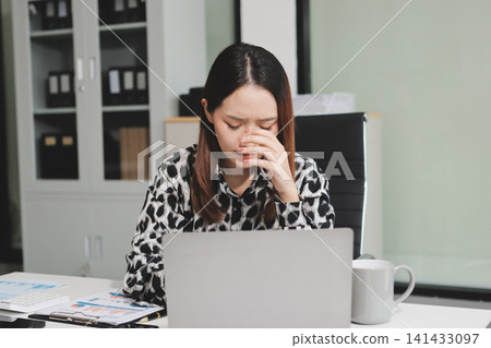 Tried young Asian office employee feeling sick and have a headache from a long working day at office Tried young Asian office employee feeling sick and have a headache from a long working day at office 141433097