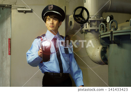 A male security guard with a flashlight patrols the basement of a building. Photo courtesy of Denpa Gakuen Educational Foundation, Tokyo Electronics College. 141433423