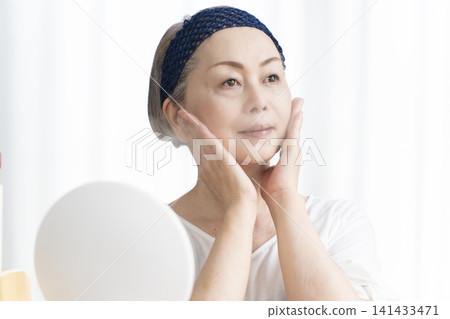 一位老年婦女使用臉部蒸氣機進行自我照顧。 一位老年婦女使用臉部蒸氣機進行自我照顧。 141433471