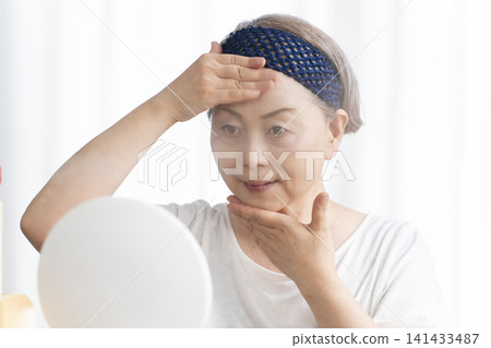 A senior woman uses a facial steamer to perform a self-care facial. A senior woman uses a facial steamer to perform a self-care facial. 141433487