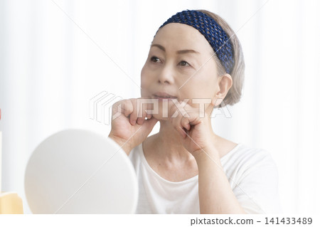 A senior woman uses a facial steamer to perform a self-care facial. A senior woman uses a facial steamer to perform a self-care facial. 141433489