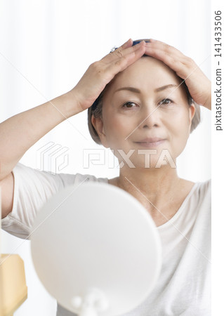 A senior woman uses a facial steamer to perform a self-care facial. 141433506
