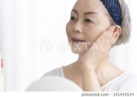 一位老年婦女使用臉部蒸氣機進行自我照顧。 一位老年婦女使用臉部蒸氣機進行自我照顧。 141433534
