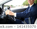 A young man in a suit, smiling, driving a company car. 141435070