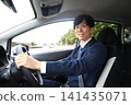 A young man in a suit, smiling, driving a company car. 141435071