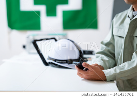 一名工人在現場辦公室看著智慧型手機。 一名工人在現場辦公室看著智慧型手機。 141435701