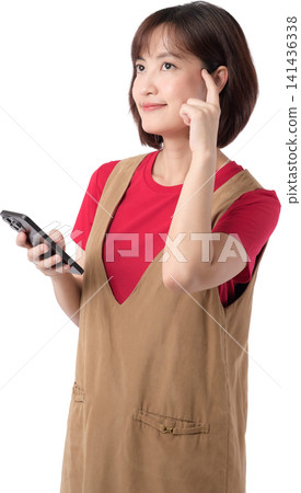 Asian woman holding smartphone with thoughtful expression isolated on transparent background posing wearing casual outfit while gesturing with finger for creative concept. PNG file format Asian woman holding smartphone with thoughtful expression isolated on transparent background posing wearing casual outfit while gesturing with finger for creative concept. PNG file format 141436338