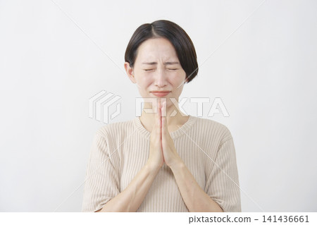 一位四十多歲的女子閉著眼睛，在白色背景前祈禱。 141436661