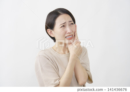 一位四十多歲的女性，在白色背景下，正忍受著牙痛的折磨。 141436676