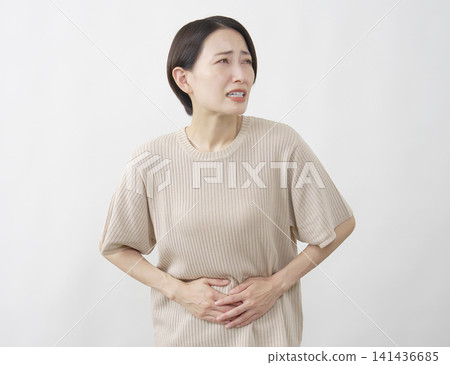 A woman in her 40s suffering from abdominal pain against a white background. 141436685