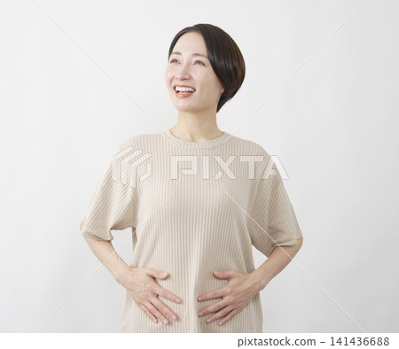 照片中，一位四十多歲的女性站在白色背景前，雙手摀著隆起的腹部。 141436688