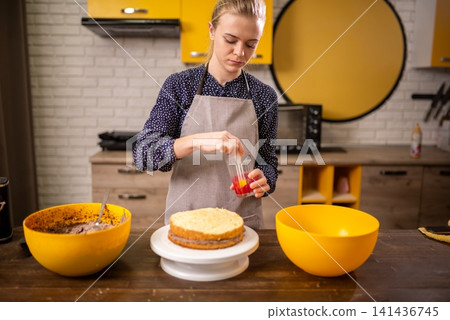 Home baker frosting round sponge cake on rotating stand in modern kitchen with bright yellow accents 141436745