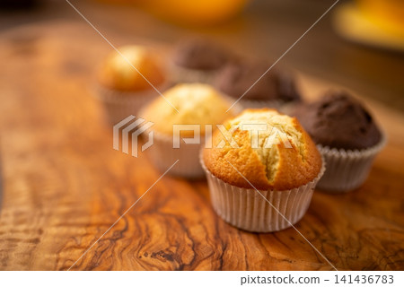 Fresh assorted muffins on wooden table with warm shallow focus lighting Fresh assorted muffins on wooden table with warm shallow focus lighting 141436783