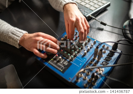 Hands adjusting knobs and sliders on a blue audio mixer in a studio Hands adjusting knobs and sliders on a blue audio mixer in a studio 141436787