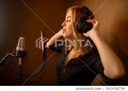 Woman singing into studio microphone with headphones in warm acoustic booth Woman singing into studio microphone with headphones in warm acoustic booth 141436794