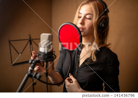 Female singer recording in professional vocal booth with pop filter and headphones Female singer recording in professional vocal booth with pop filter and headphones 141436796