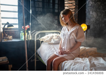 Lonely female patient sitting on a bed next to an IV drip Lonely female patient sitting on a bed next to an IV drip 141436808
