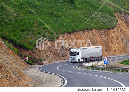 Truck navigates sharp turn on mountain road through grassy terrain Truck navigates sharp turn on mountain road through grassy terrain 141436882