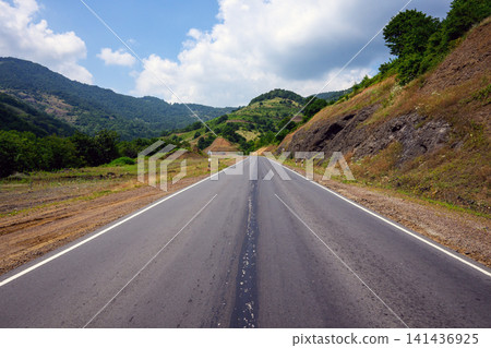 Empty asphalt road between rolling hills under bright sky Empty asphalt road between rolling hills under bright sky 141436925