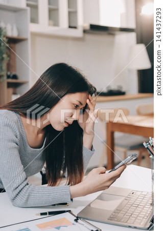 Young Asian woman sits at office desk rubbings her eyes and temples feeling pain. Stress. And exhaustion from long hours working on the computer 141437293