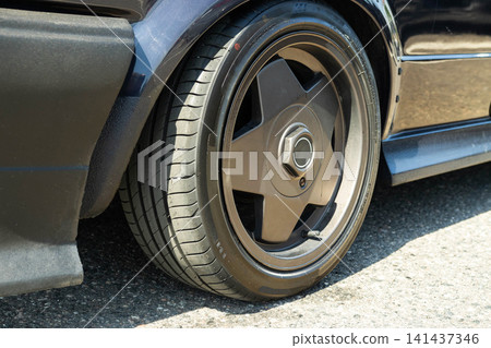 Close up detail view of a modern performance car wheel and tire on a dark blue vehicle with custom body kit, showcasing automotive tuning and design 141437346