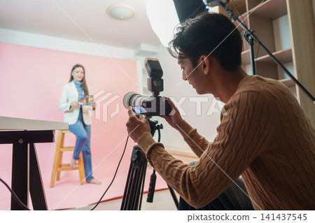 Asian photographer taking photos of female model in professional studio Asian photographer taking photos of female model in professional studio 141437545