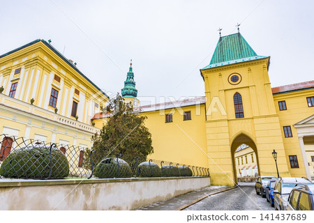 A winter scene featuring the historic gate of Kroměříž Castle, a UNESCO World Heritage Site, and its snow-covered yellow walls and towers. 141437689