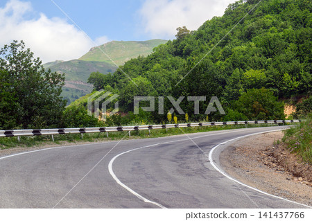 Mountain road curves through forest with guardrail and clear sky Mountain road curves through forest with guardrail and clear sky 141437766
