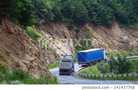 Trucks travel along curved mountain road surrounded by greenery Trucks travel along curved mountain road surrounded by greenery 141437768