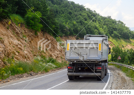 Dump truck navigates steep mountain road with forested slopes Dump truck navigates steep mountain road with forested slopes 141437770