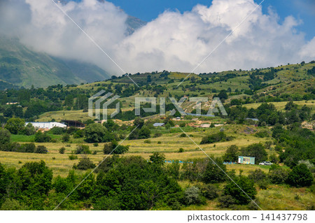 Mountain valley landscape with clouds, green slopes, and small farmhouses Mountain valley landscape with clouds, green slopes, and small farmhouses 141437798