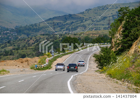 Three cars navigate winding road through forested mountainside Three cars navigate winding road through forested mountainside 141437804