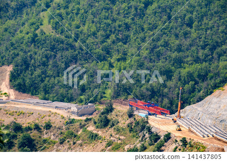 Construction equipment digs into hillside covered in green forest Construction equipment digs into hillside covered in green forest 141437805
