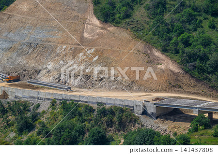 Road under construction across rocky terrain with green forest surroundings 141437808