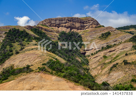 Dry, rocky mountain terrain with scattered green shrubs under clear sky Dry, rocky mountain terrain with scattered green shrubs under clear sky 141437838