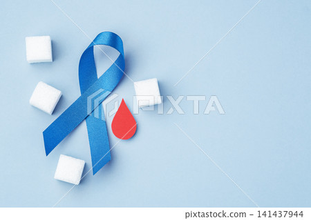 Blue ribbon with sugar cubes and red blood drop on blue background, World Diabetes Day concept, copy space Blue ribbon with sugar cubes and red blood drop on blue background, World Diabetes Day concept, copy space 141437944