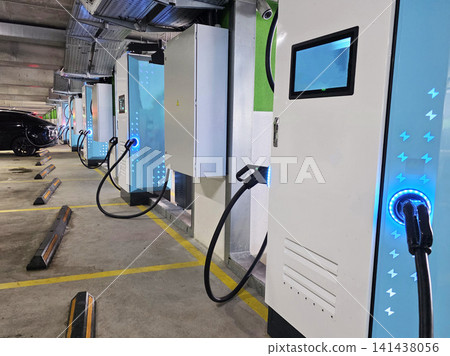Electric vehicle charging stations with glowing blue lightning bolt symbols power a car in a modern underground parking garage, highlighting advanced sustainable transportation technology. Electric vehicle charging stations with glowing blue lightning bolt symbols power a car in a modern underground parking garage, highlighting advanced sustainable transportation technology. 141438056