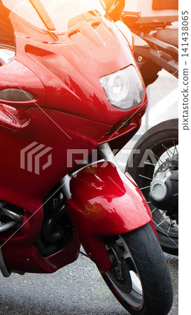 Red sport motorcycle parked on asphalt street, front fairing and headlight visible, raindrops on bodywork, bright sunlight creates warm lens flare effect, modern vehicle design Red sport motorcycle parked on asphalt street, front fairing and headlight visible, raindrops on bodywork, bright sunlight creates warm lens flare effect, modern vehicle design 141438065