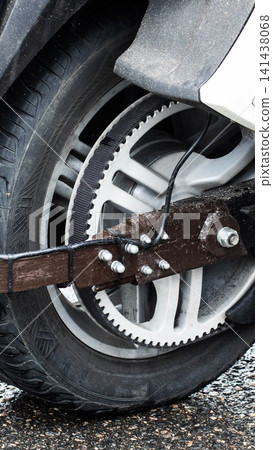 Close-up of motorcycle rear wheel and drive belt system, showing mechanical detail of custom brown component secured by bolts and zip ties on wet asphalt surface 141438068